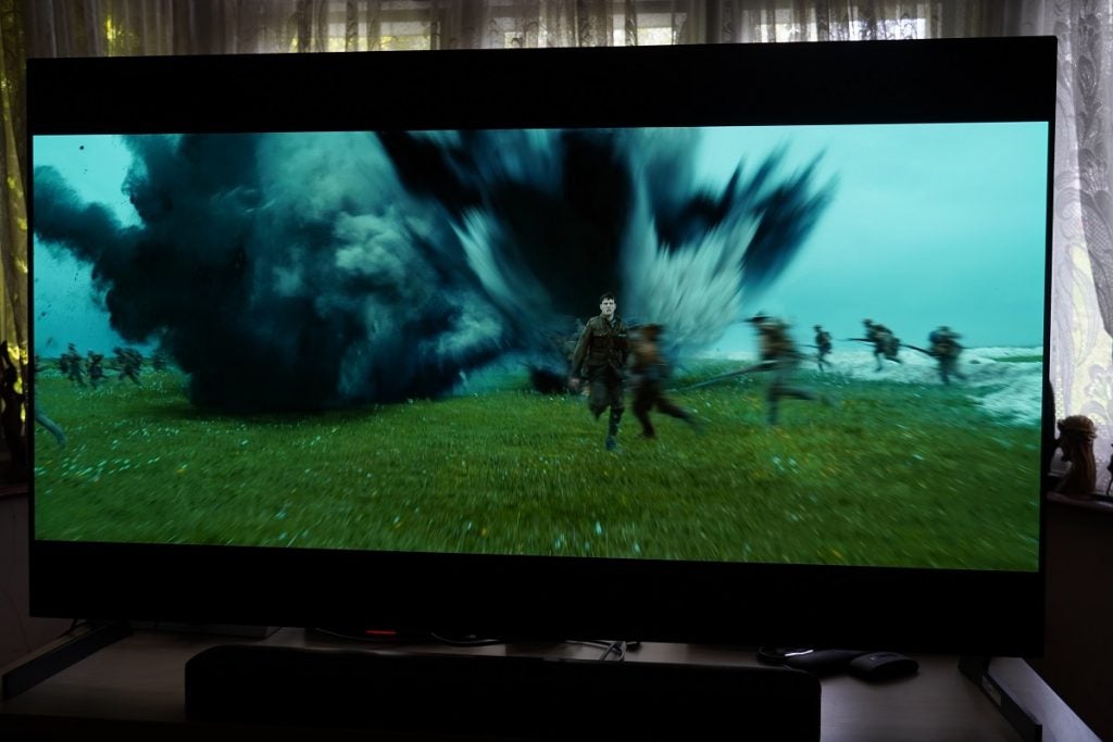 1917 on the LG G1 OLEDLG G1 OLED TV playing a movie, displaying men running to the left on a grassy field, a bomb explosion from which a man is running away