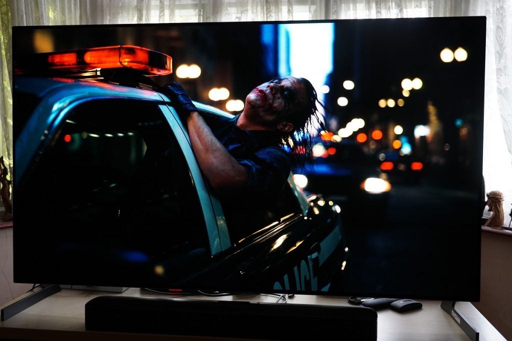 The Dark Knight on the LG G1 OLEDLG G1 OLED TV playing a movie, displaying  a joker painted face man pushing half of his body through window of a Police car