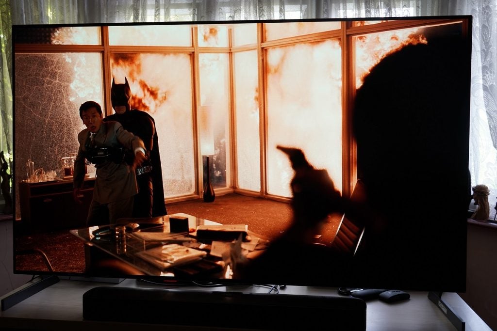 LG G1 OLED TV playing a movie, displaying  a man pointing a gun towards a man held by Batman and fire behind him