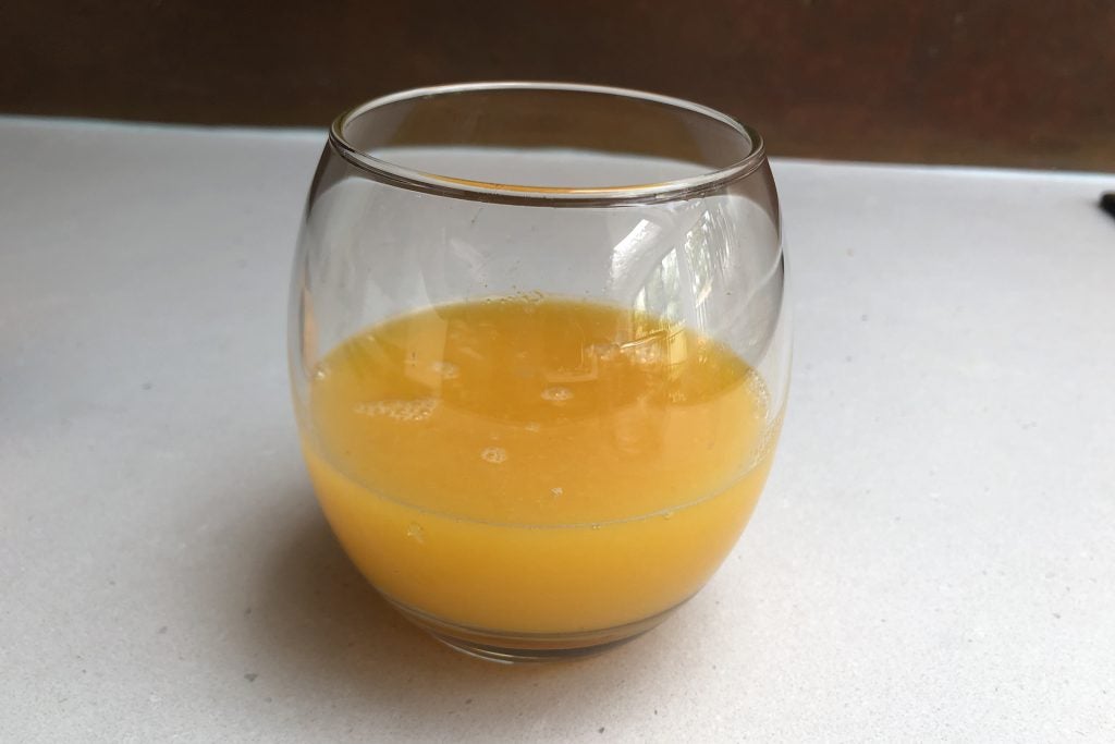 Fresh orange juice in a clear glass on a white surface.