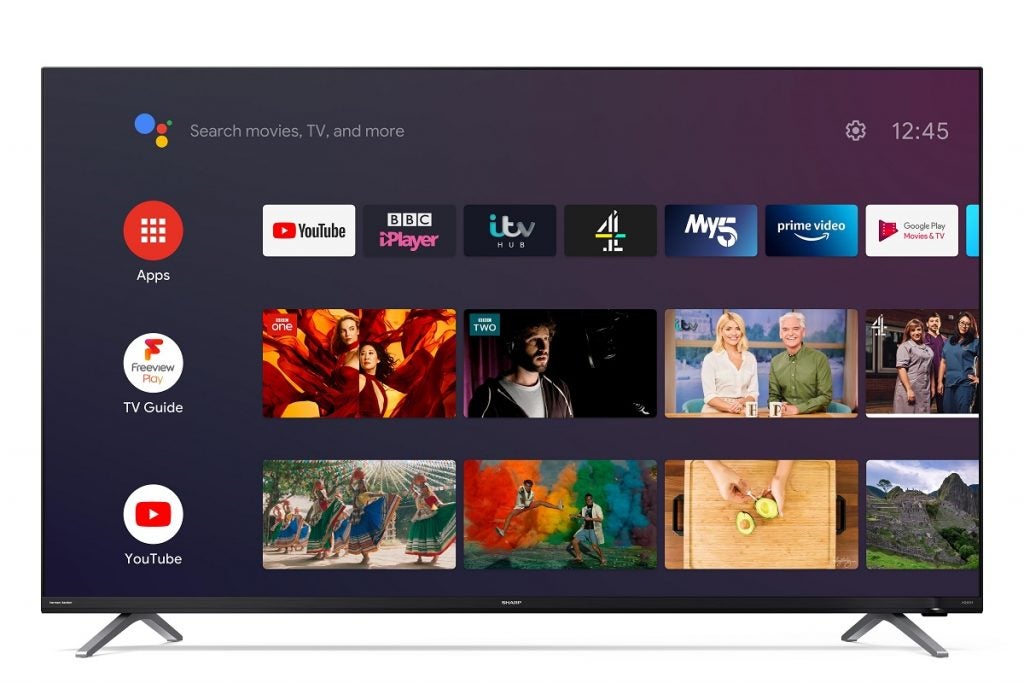 Sharp 50KU 4FE C1 TV with stand displaying apps, TV guide and youtube section with a setting button on the top lleft and Google assistant search bar on top right