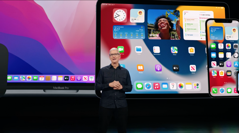 Tim cook in a black outfit, joined hands, standing with Macbook Pro, iPad and iPhone at the back on the screen