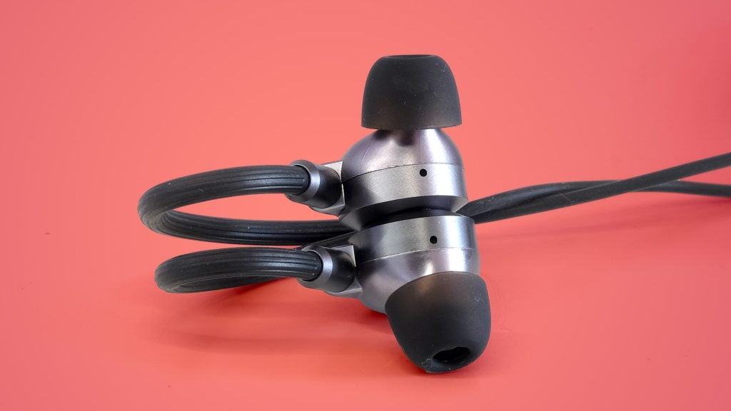 Ausounds AU-Flex ANC earbud housings magnetically connectedAusound earphones resting on a reddish pink table, buds stick together via magnet at their backAusound earphones resting on a reddish pink table, buds stick together via magnet at their back