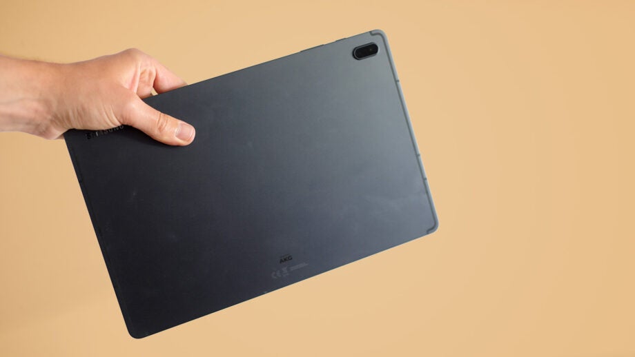 Hand holding Samsung Galaxy Tab S7 FE tablet against beige background.