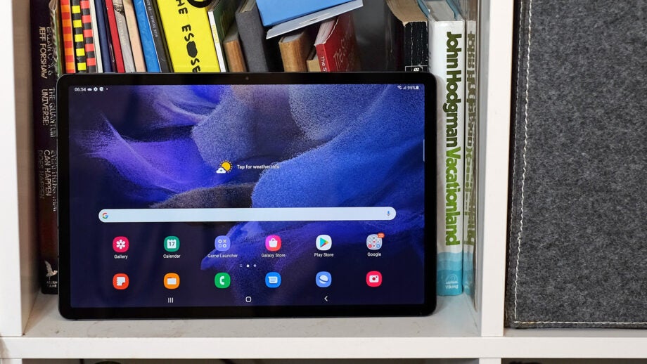 Samsung Galaxy Tab S7 FE on a bookshelf displaying home screen.