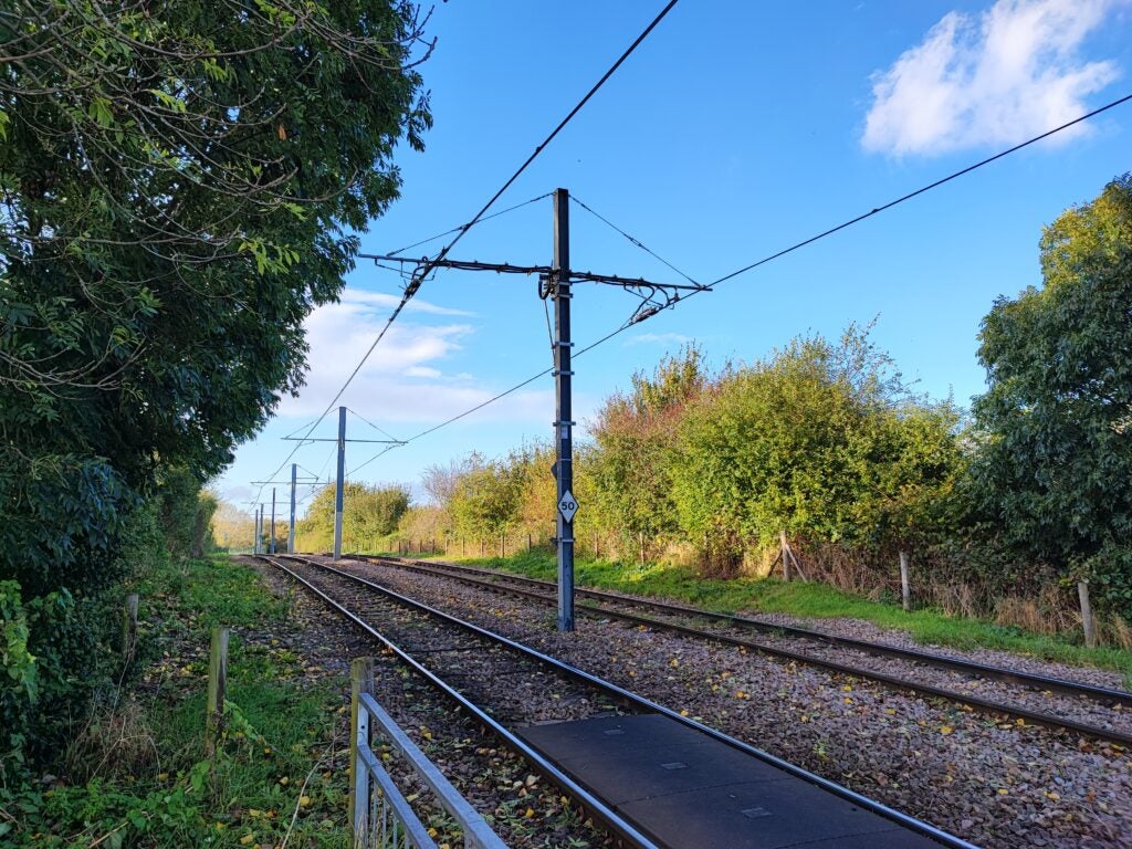 Railway track surrounded by greenery under a blue sky.