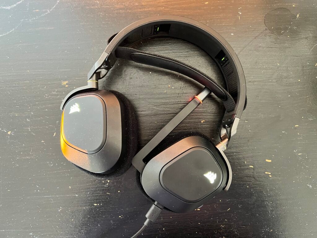 Headset Corsair HS80 RGB tergeletak di atas meja hitam