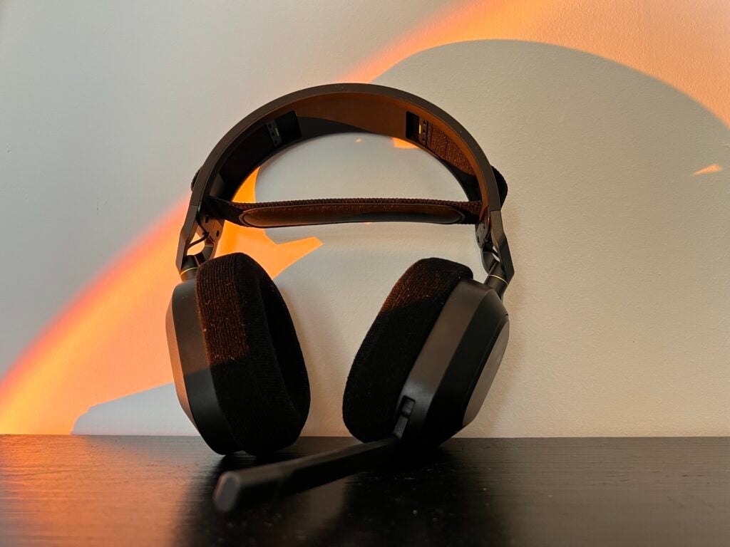 O headset Corsair HS80 RGB encostado em uma parede em uma mesa preta