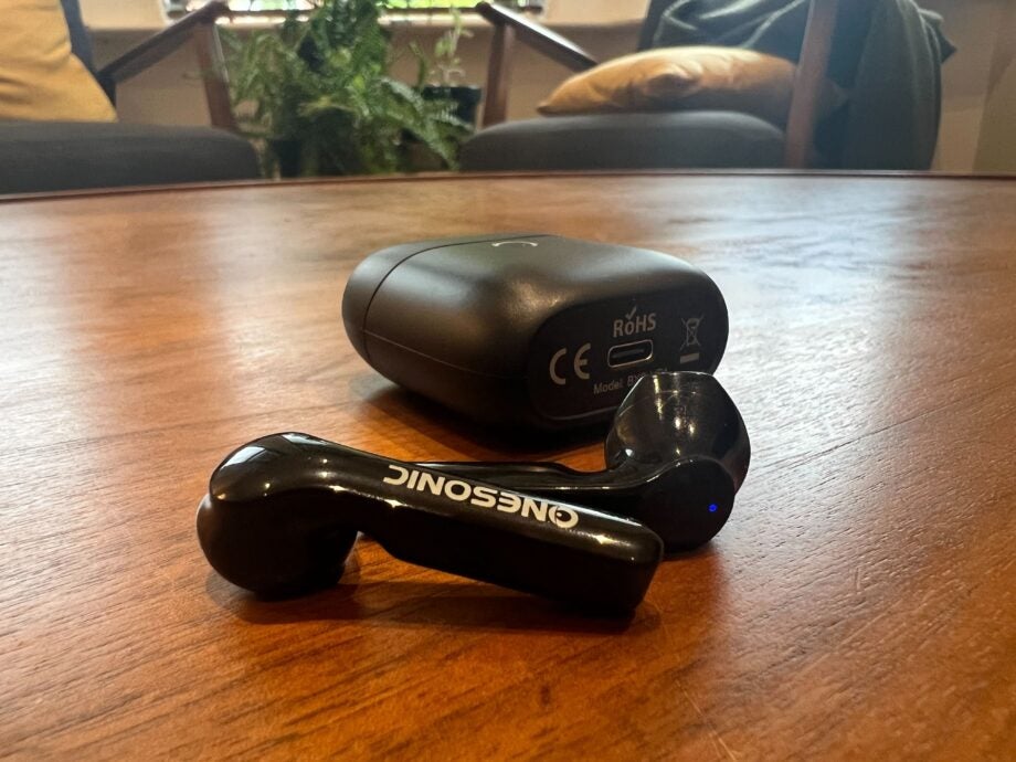 The OneSonic earbuds lay flat on the table with the charging case