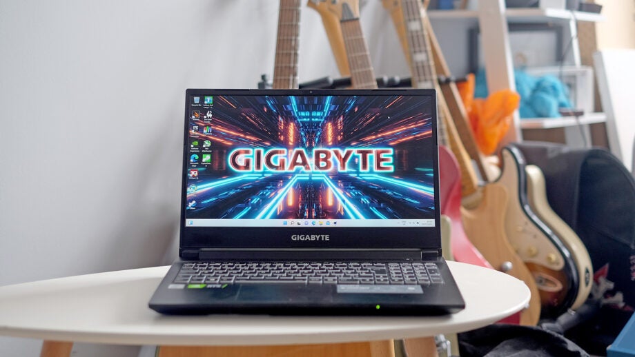 Gigabyte G5 gaming laptop on desk with guitars in background