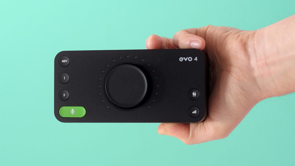 Hand holding Audient Evo 4 audio interface against teal background.