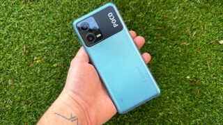 Hand holding Poco X5 5G smartphone over grass.