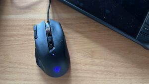 AOC Agon AGM600 gaming mouse on wooden desk beside laptop.