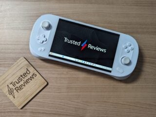 Ayaneo 2S handheld gaming PC on wooden desk with Trusted Reviews on screen.