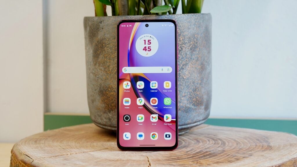 Moto G84 5G screen in front of a plant potMotorola Moto G84 5G smartphone on wooden surface.