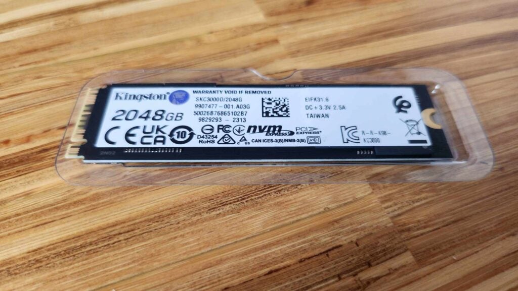 Kingston KC3000Kingston KC3000 2048GB NVMe SSD on wooden surface.