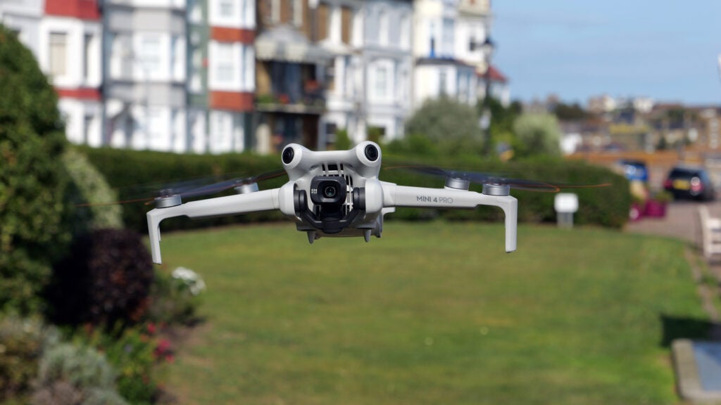DJI Mini 4 Pro mid flightDJI Mini 4 Pro drone flying with homes in background.