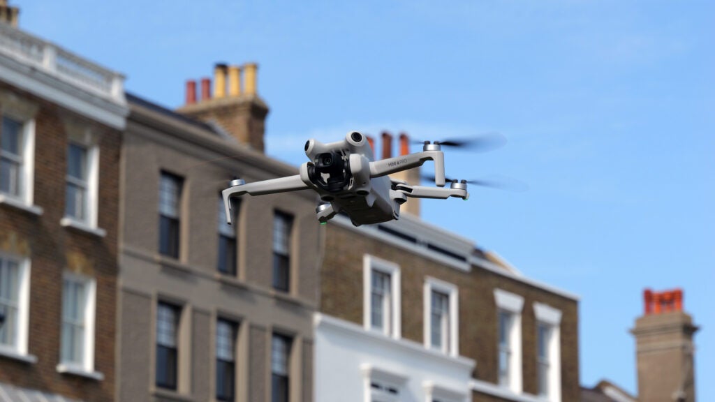 DJI Mini 4 Pro mid-flightDJI Mini 4 Pro drone flying in front of buildings.