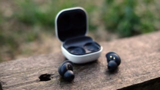 Samsung Galaxy Buds FE on wooden surface with open case.