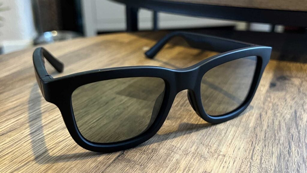 The Ampere Dusk smart sunglasses seen from a straight-facing angle on a wood table with dimming turned off.