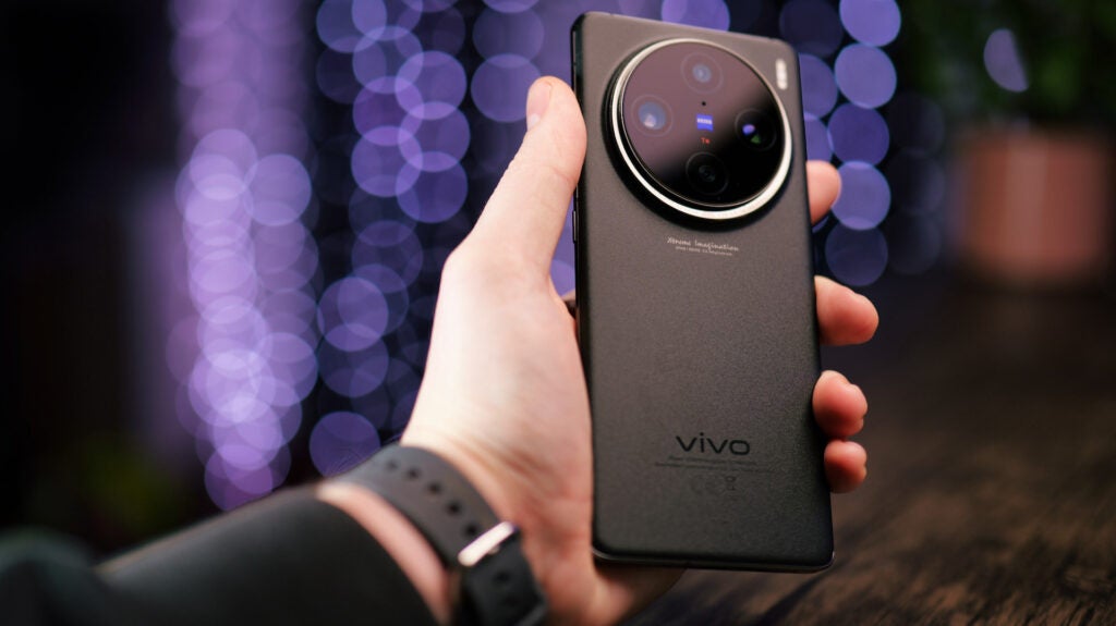 Vivo X100 Pro in-handHand holding Vivo X100 Pro smartphone with bokeh background.