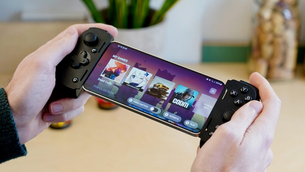 ゲームが表示されたスマートフォンに接続された Razer Kiyo V2 Pro を持っている手。