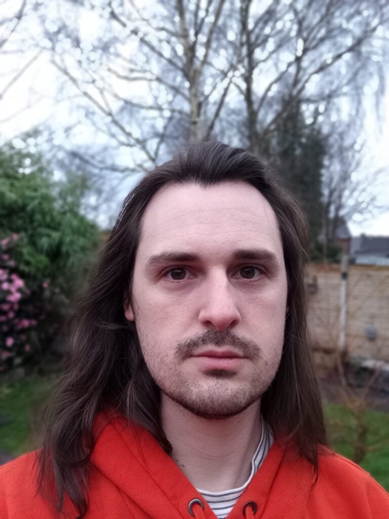 TCL 40 Nxtpaper 4G selfie camera sampleThis image is unrelated to the TCL 40 Nxtpaper 4G or its product review.Person with long hair and a red hoodie outdoors.