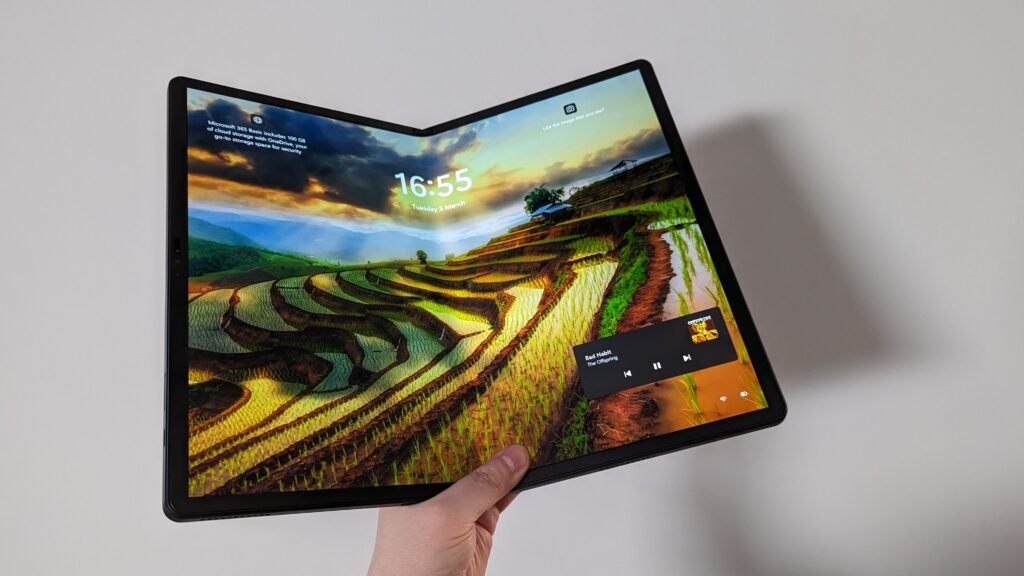 Hand holding Lenovo ThinkPad X1 Fold with landscape wallpaper.